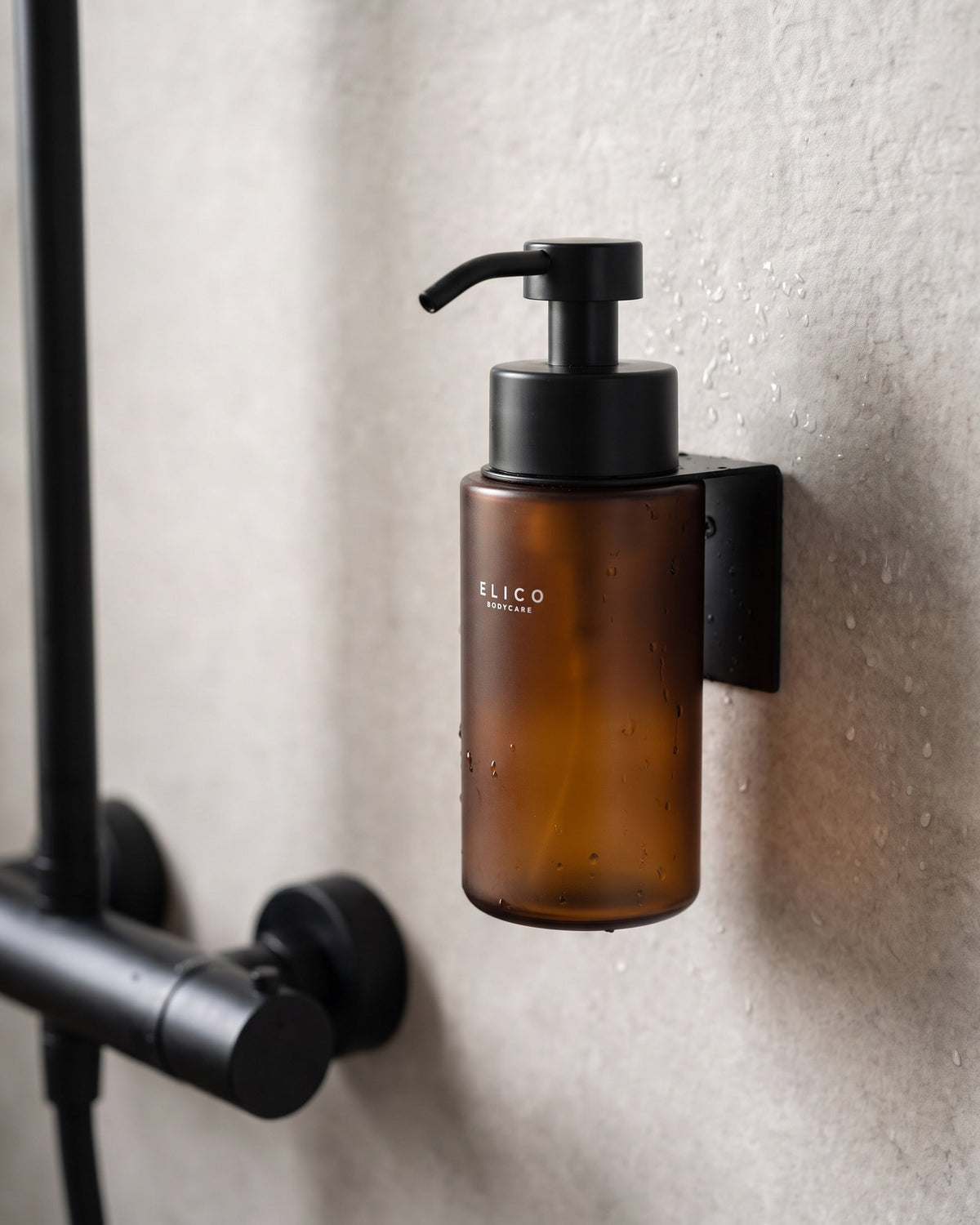 Ravbrun Elico Bodycare-dispenser i det matt svarta väggfästet i duschen, bredvid en svart blandare