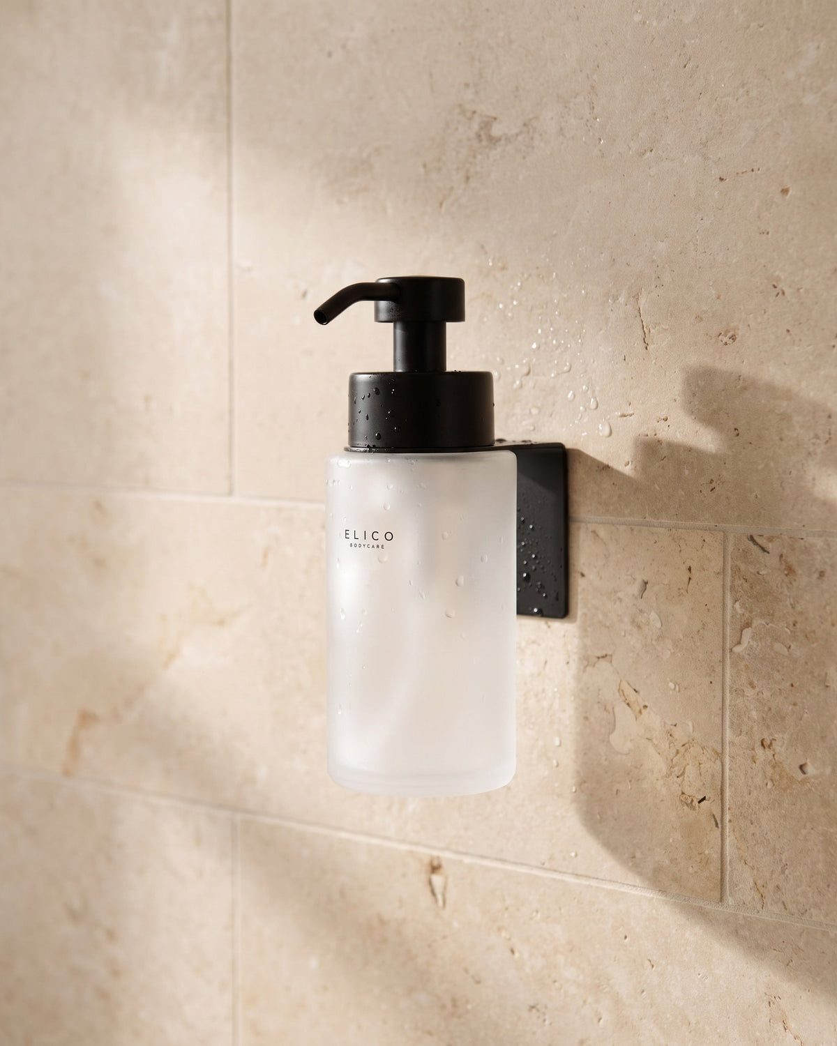 Frostad Elico Bodycare-dispenser i det matt svarta väggfästet på en kalkstensvägg i duschen